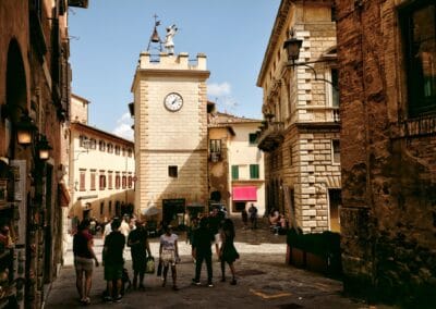 a group of people standing in a courtyard with a clock tower in Montepulciano