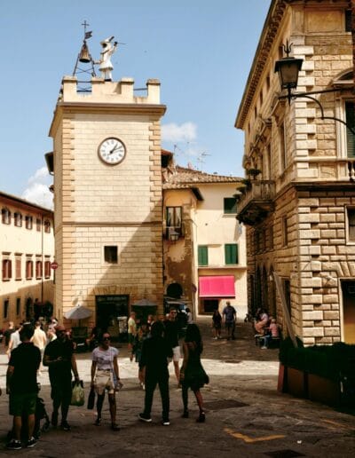 a group of people standing in a courtyard with a clock tower in Montepulciano